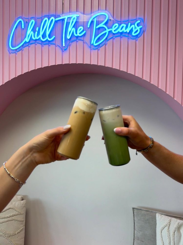 Two iced drinks touched together under the neon Chill The Beans sign