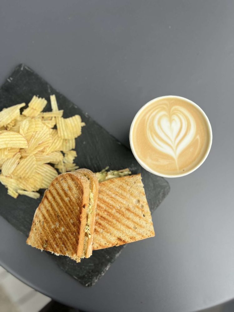 Toasted sandwich and crisps on slate, with a latte