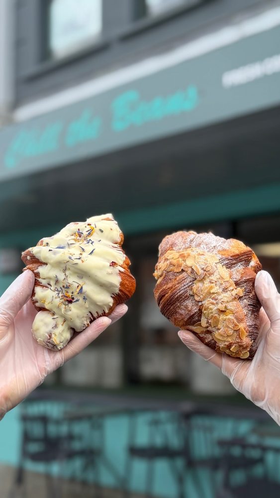 Two pastries held up in front of the teal shopfront